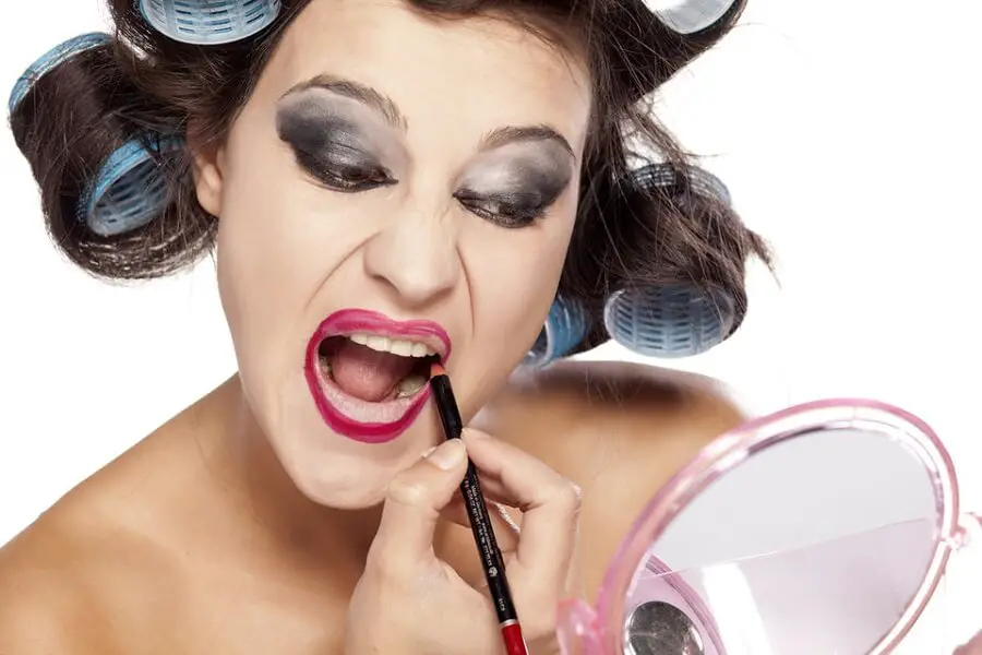 woman looking in the mirror while applying a lot of harsh makeup
